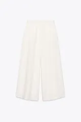 Pantalón blanco de tiro alto con pinzas delanteras, bolsillos laterales y pernera ancha. Cierre lateral con cremallera oculta.