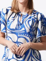 Blusa de seda fría con estampado abstracto en blanco y azul. Tiene cuello redondo con frunce, escote en V con botón y mangas cortas amplias.