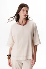 Blusa de lino color beige claro, con mangas 3/4 y cuello redondo. Presenta pespuntes a contratono en el centro, puños y ruedo.