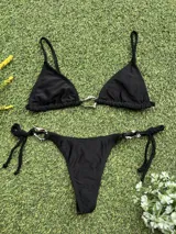 Conjunto de bikini negro con corpiño triangular con argolla metálica y bombacha colaless con tiras para atar y argollas en los costados.