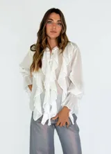 Camisa blanca traslúcida con volados frontales, cuello mao y mangas largas con puños fruncidos.