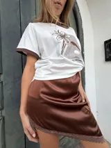 Remera blanca de algodón y spandex con cuello y mangas con ribete marrón. Estampado frontal con diseño floral y texto. Detalles bordados.