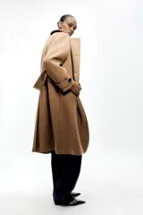 Abrigo color camel confeccionado en hilatura con lana. Tiene cuello solapa, manga larga, bolsillos delanteros ocultos en costura y cierre frontal cruzado con botones negros.
