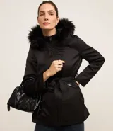 Campera parka negra con cuello alto, capucha con borde de piel sintética, cierre frontal con cremallera, bolsillos con cremallera y cinturón con hebilla.