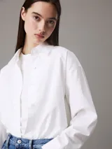 Camisa blanca de algodón Oxford, corte relaxed, cuello en punta, manga larga con puños abotonados y bajo redondeado.