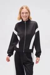 Campera deportiva negra con cierre frontal, cuello alto y detalles de recortes curvos blancos en mangas y laterales.