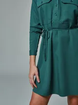 Vestido camisero verde con cuello clásico, mangas largas, cierre frontal con botones, dos bolsillos con solapa en el pecho y cinturón con lazo.
