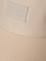 Gorro color crema con visera curva y parche cuadrado con logo en el frente.