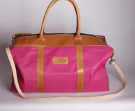 Bolso de lona color fucsia combinado con detalles de cuero, con asas y correa ajustable.