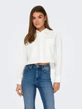 Camisa blanca de corte cropped, con cuello clásico, mangas largas con puños abotonados y dos bolsillos de parche en el pecho.