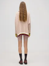 Sweater tejido de algodón color rosa claro, con cuello polo con cierre de cremallera metálica y mangas largas con puños a rayas de colores.