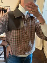 Campera corta a cuadros color marrón, negro y blanco, con cuello de cuero marrón, cierre con botones y mangas largas.