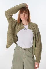 Cardigan color crudo de tejido de punto con diseño trenzado, cuello alto y cierre frontal con cremallera.