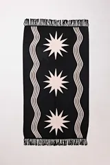 Pareo playero rectangular negro con estampado de estrellas y líneas onduladas en color crema, con flecos en los extremos.