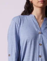 Blusa celeste texturada marca Ninety, con cuello a la base, escote en V y abertura central con botones. Delantera con bolsillo y mangas tres cuartos regulables con presilla y botón.