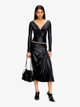 Bolso tipo cubo para mujer con forma fruncida y acabado en cuero brillante. Presenta el logotipo 'D' metálico en el centro y cordones ajustables con detalles metálicos. Incluye múltiples bolsillos internos.