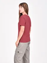 Remera blanca de manga corta con cuello redondo y un estampado artístico en tonos rojo oscuro y negro que simula una figura femenina con pantalón ancho a rayas.