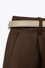 Bermuda color crema de tiro medio con pinzas delanteras y cinturón fino color beige. Tiene bolsillos frontales y falsos bolsillos de vivo en la espalda.