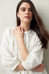 Camisa blanca a rayas grises, de corte amplio, cuello mao y mangas 3/4 con puños abotonados.