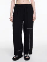 Pantalón negro de lino con elástico en la cintura y calce relajado. Incluye bolsillos laterales y un bolsillo invertido. Detalles de bordado tipo pespunte en color gris recorren la pierna y el bajo.