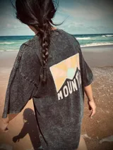 Remera negra con efecto gastado, corte holgado y estampa en la espalda con montañas y la palabra "Mountain" en blanco.