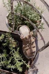 Sandalia de cuero color beige con tiras anchas entretejidas, hebilla lateral y suela plana.