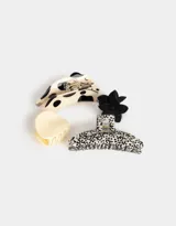 Set de cuatro broches para el pelo con diferentes diseños: uno con forma de mandíbula con estampado de vaca, uno con forma de mandíbula liso color crema, uno con forma de flor negro y uno con forma de mandíbula con estampado de leopardo.
