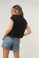 Camiseta negra con textura acanalada, corte holgado y cuadrado, cuello en punta, bolsillos amplios y botones funcionales.