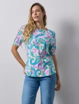 Remera estampada con diseño paisley en tonos celeste, rosa, amarillo y verde. Tiene mangas cortas con detalle de aberturas y lazos en los hombros.