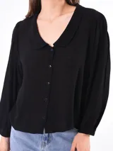 Camisa negra con cuello bebé, manga larga abullonada y cierre frontal con botones.