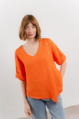 Blusa color naranja confeccionada en 100% lino, con escote en V, mangas cortas con vuelta y silueta amplia. Presenta terminación asimétrica y fila de botones decorativos en uno de los hombros.
