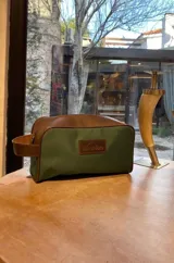 Neceser de lona verde con detalles en cuero color beige y etiqueta con logo de la marca Sierra Mora.