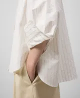 Camisa blanca de algodón con finas rayas verticales. Tiene cuello solapa, cierre con botones, manga larga con puño, bolsillo en el pecho y canesú en la espalda.