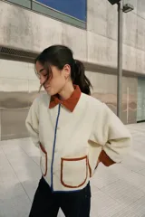 Campera color crema de corderito con cuello y ribetes en color marrón y detalles en azul.