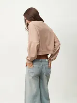 Buzo corto color beige con cuello redondo y mangas largas.