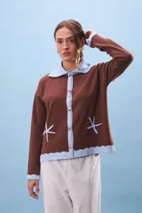 Cárdigan marrón de tejido de punto con cuello polo celeste, cierre frontal con botones y dos estrellas de mar bordadas.