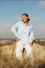 Camisa celeste a rayas verticales blancas, de corte holgado, con cuello camisero y cierre frontal con botones.