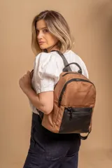 Mochila urbana color tostado con detalles en símil cuero negro. Cuenta con un amplio compartimento principal con cierre, un bolsillo frontal con cierre y correas ajustables.