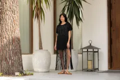 Vestido negro de algodón con corte recto, cuello redondo, mangas cortas, tachas plateadas en el frente y flecos largos en el ruedo.