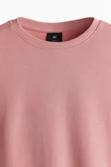 Buzo rosa de tejido liviano de mezcla de algodón con interior cepillado suave, cuello redondo ribeteado, hombros caídos y remate ancho acanalado en puños y bajo. Corte holgado.