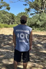 Remera sin mangas de algodón con lavado acid wash, color azul. Estampado grande en la espalda con el texto "MEDITERRANEAN HOT SEASON", donde la letra 'O' de 'HOT' es reemplazada por un sol estilizado.