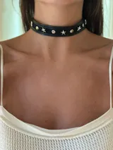 Gargantilla tipo choker de cuero sintético negro, con apliques de estrellas y remaches plateados. Se cierra con cadena y mosquetón para ajustar el largo.