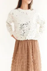 Sweater color beige de tejido de punto con cuello redondo y mangas largas. Presenta apliques de lentejuelas plateadas en el frente y las mangas.