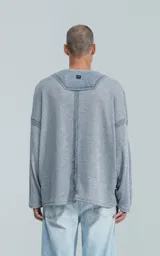 Sweater de manga larga color gris jaspeado, con cuello redondo. Presenta costuras externas decorativas y marcadas en los laterales del cuerpo y en la unión de las mangas, dándole un aspecto técnico o deconstruido.