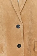 Blazer color camel confeccionada en piel de ante 100%. Diseño clásico con cuello solapa, escote pico, manga larga, bolsillos con solapa en delantero, forro interior combinado, bajo con abertura en espalda y cierre frontal con botones.