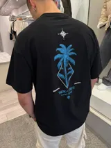 Remera negra de algodón con estampado en la espalda de una palmera azul dentro de un rombo y una brújula en la parte superior.
