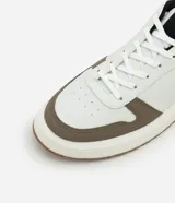 Championes casuales de material sintético color blanco con recortes en marrón, negro y beige. Presentan puntera redonda, cordones y suela contrastante color caramelo.