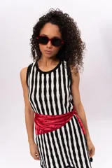 Vestido tejido de punto con rayas verticales en blanco y negro, sin mangas y con abertura en la espalda. Incluye un pañuelo rojo con lunares negros atado a la cintura.