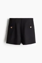 Short negro de tiro alto en punto interlock pesado con elástico oculto en la cintura y pinzas moldeadoras. Presenta bolsillos delanteros decorativos con botón de metal dorado.