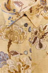 Camisa de ramio color beige con estampado floral en tonos marrones y azules, cuello solapa, manga larga con puños abotonados, bajo asimétrico con aberturas laterales y cierre frontal con botones.